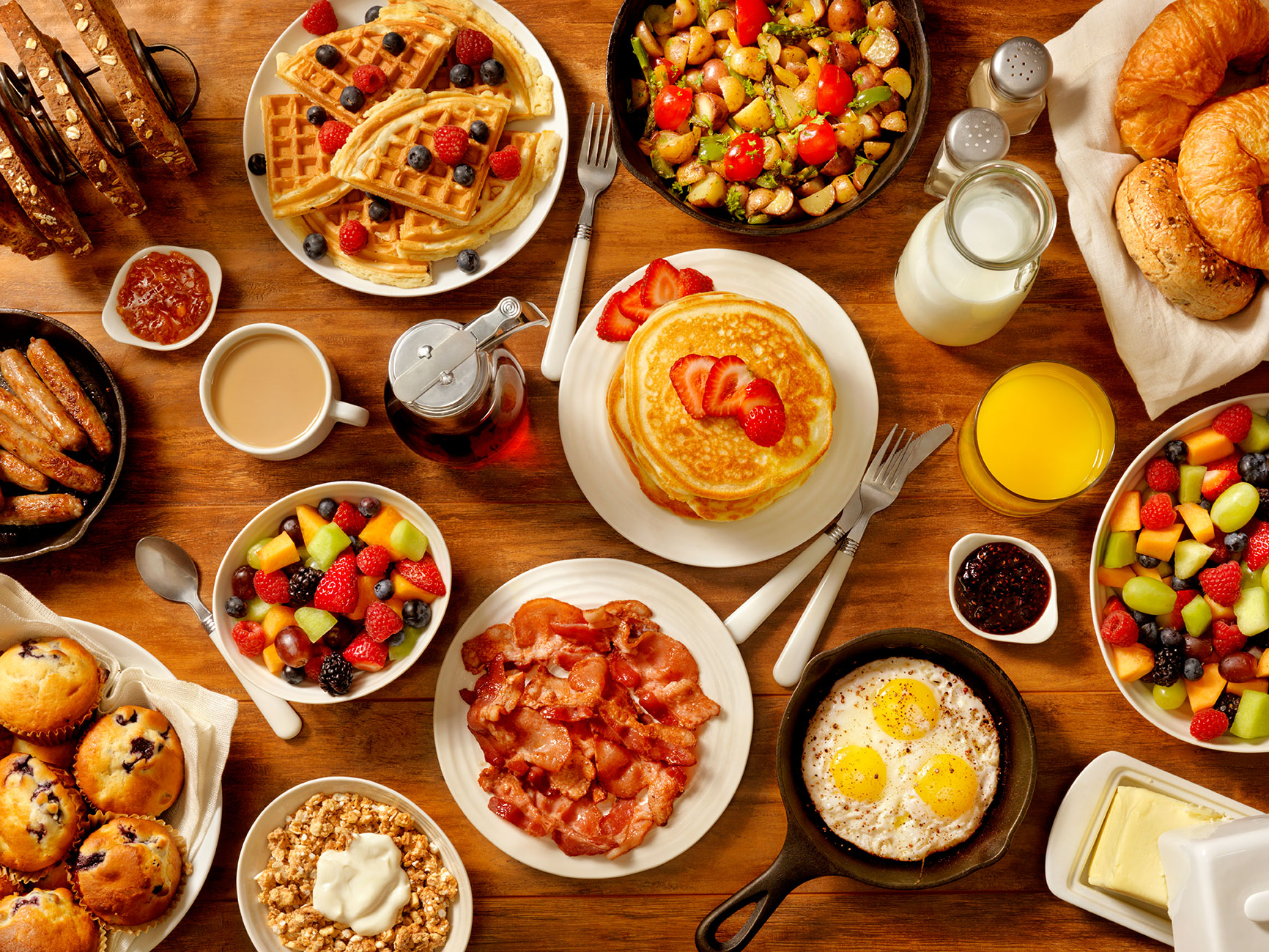 Tisch vollgedeckt mit Speck, Pfannkuchen, Fruchtsaft, Obst, Honig, Muffins, Eier